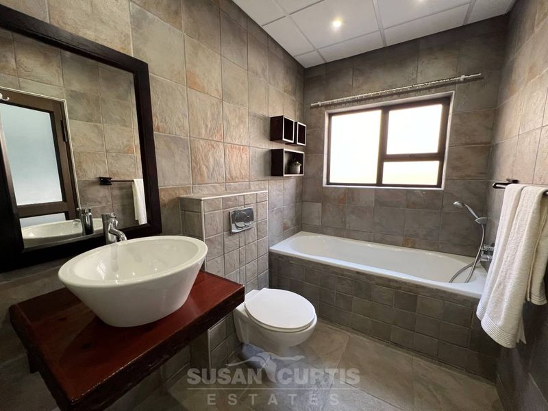 A well-maintained bathroom featuring a vessel sink, wall-mounted toilet, and a built-in bathtub with tiled finishes throughout.