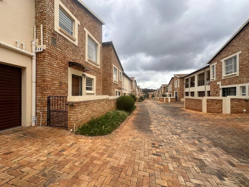 A view of the townhouse complex street featuring face brick facades, paved driveways, and secure access points.