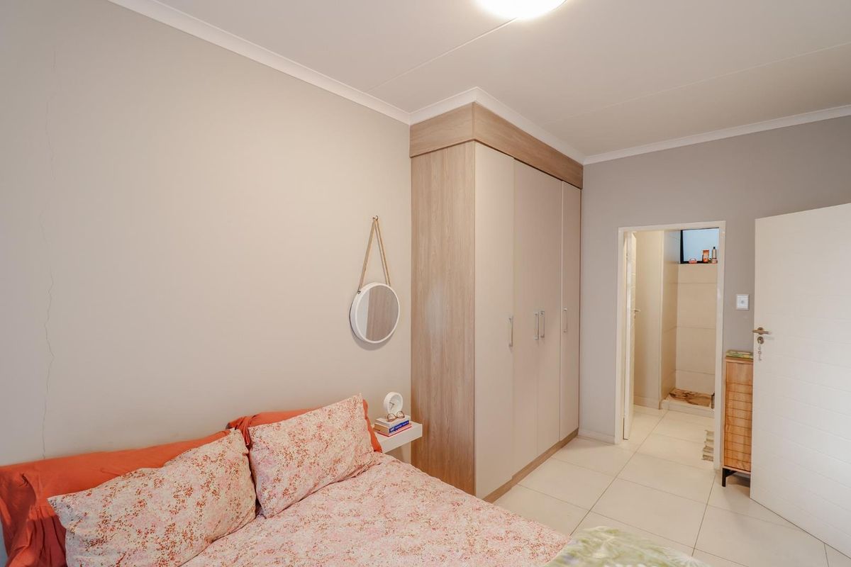 A well-maintained bedroom featuring built-in wooden cabinetry and tiled flooring, with an adjoining doorway leading to a bathroom area.