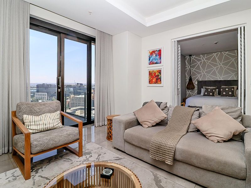 Modern living room featuring large sliding glass doors with city views and seamless access to the adjacent bedroom through bi-fold doors.
