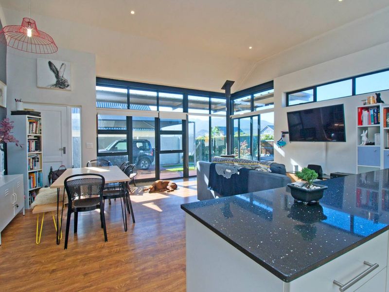 Spacious open-plan living and dining area featuring vaulted ceilings, large glass doors for natural light, and a modern kitchen with black granite countertops.
