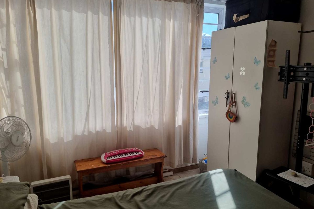 A bedroom featuring a large window with curtains and a built-in wardrobe, providing natural light and storage space.