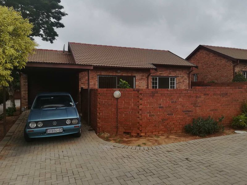 Front view of a single-story brick townhouse featuring a tiled roof, paved driveway, and a private carport.