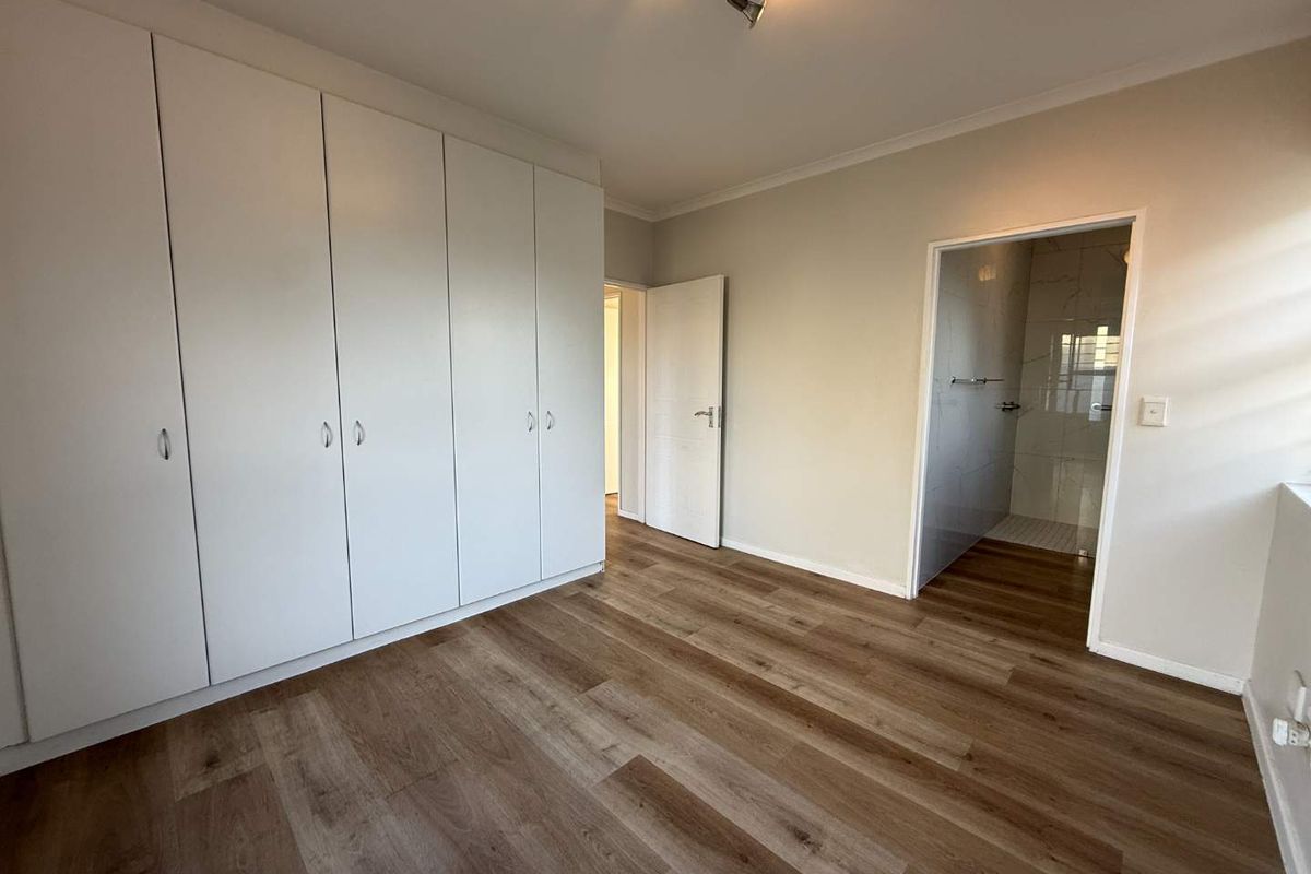 A clean, empty bedroom featuring modern laminate flooring, extensive built-in cupboard storage, and direct access to an en-suite bathroom.