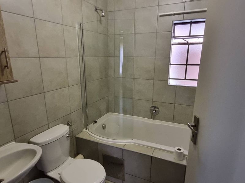 A functional bathroom featuring tiled walls, a bathtub with a glass shower screen, a pedestal basin, and a wall-mounted medicine cabinet.