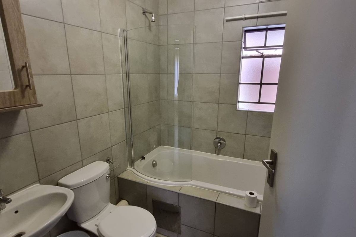 A functional bathroom featuring tiled walls, a bathtub with a glass shower screen, a pedestal basin, and a wall-mounted medicine cabinet.