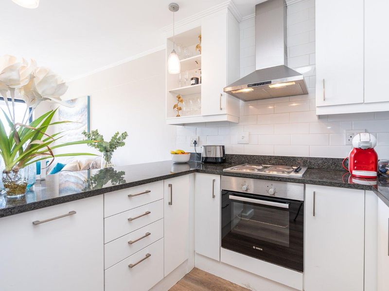 Modern kitchen featuring white cabinetry, granite countertops, subway tile backsplash, and integrated stainless steel appliances including an oven and extractor fan.