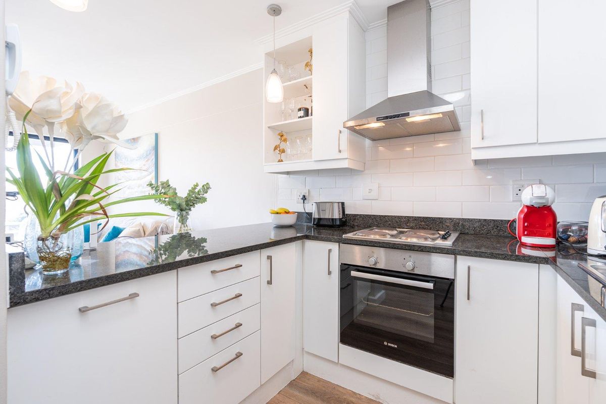 Modern kitchen featuring white cabinetry, granite countertops, subway tile backsplash, and integrated stainless steel appliances including an oven and extractor fan.