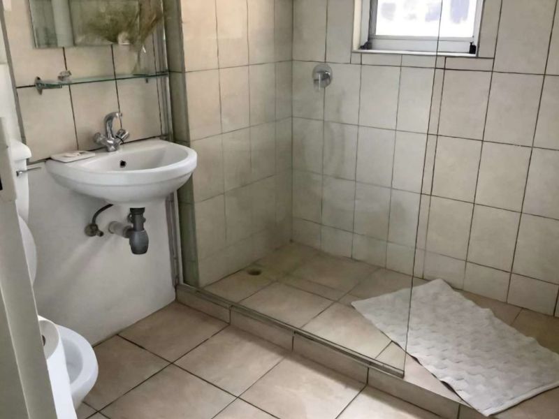 A functional bathroom featuring a wall-mounted basin, a glass-enclosed shower, and tiled surfaces throughout.