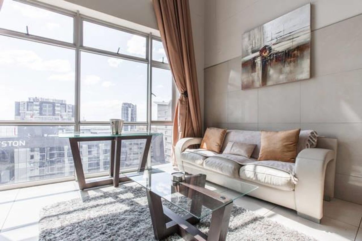 Bright living area featuring large floor-to-ceiling windows with city views, neutral tiled flooring, and a modern tiled feature wall.