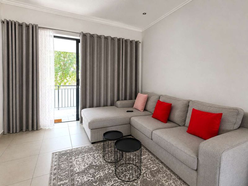 A bright living room featuring neutral tiled flooring, recessed lighting, and a sliding glass door providing access to an outdoor balcony area.