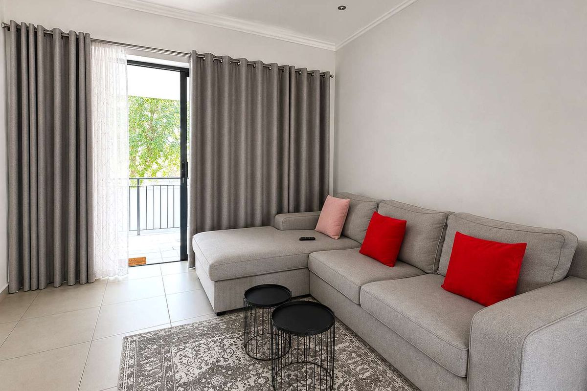A bright living room featuring neutral tiled flooring, recessed lighting, and a sliding glass door providing access to an outdoor balcony area.