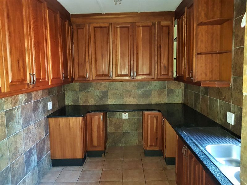 A functional kitchen featuring wooden cabinetry, granite countertops, tiled backsplash, and a stainless steel sink.