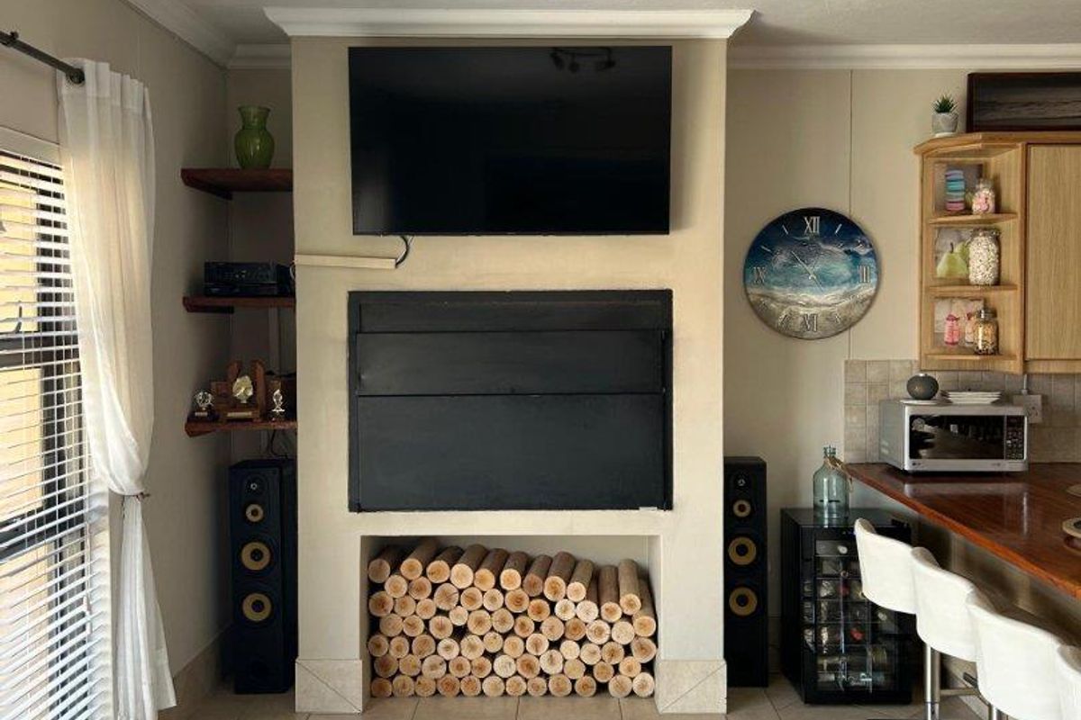 A living area featuring a built-in fireplace with integrated log storage, adjacent wooden shelving, and a breakfast bar counter.