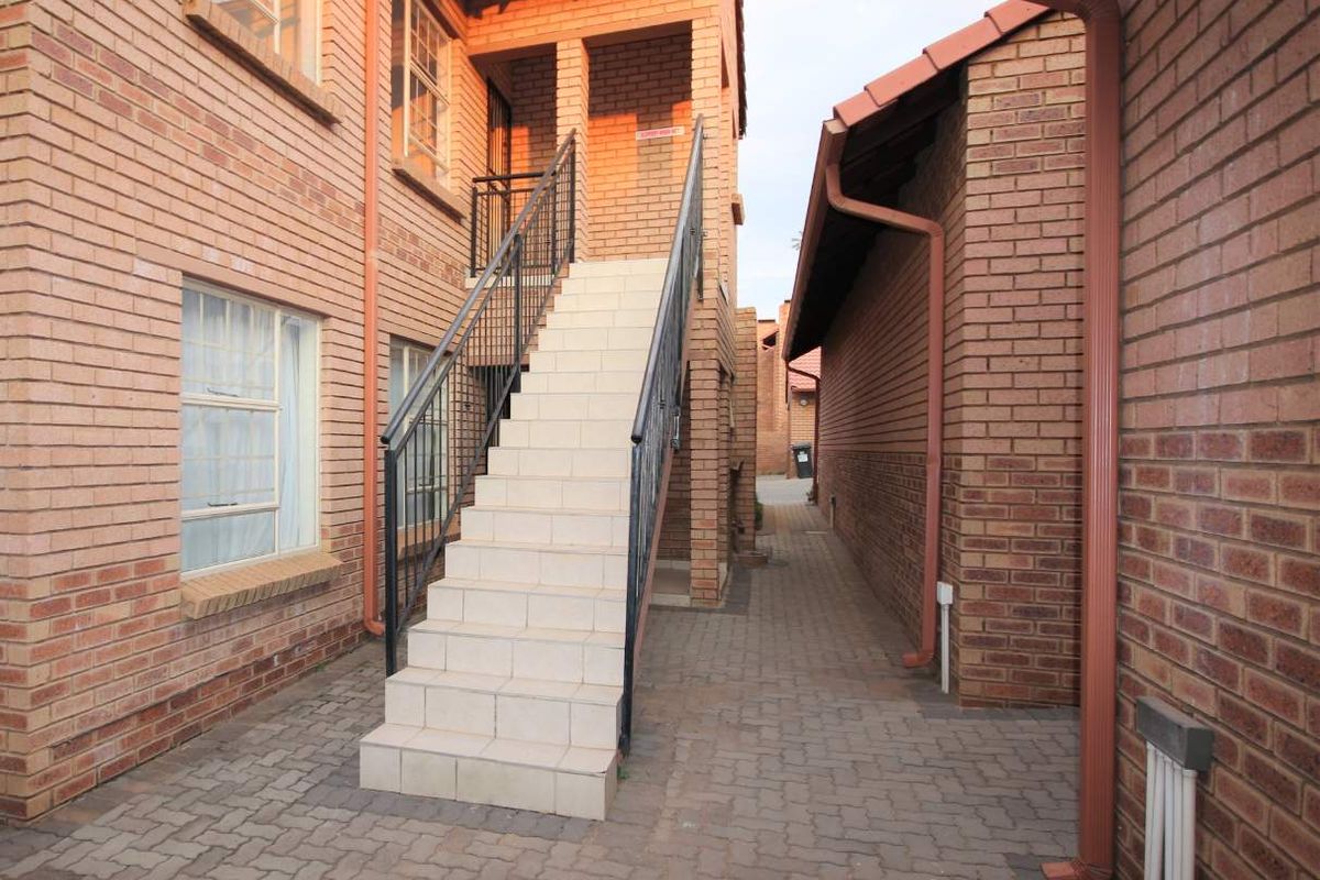 Exterior view of an apartment complex featuring a paved courtyard, face brick walls, and an external tiled staircase with metal railings.