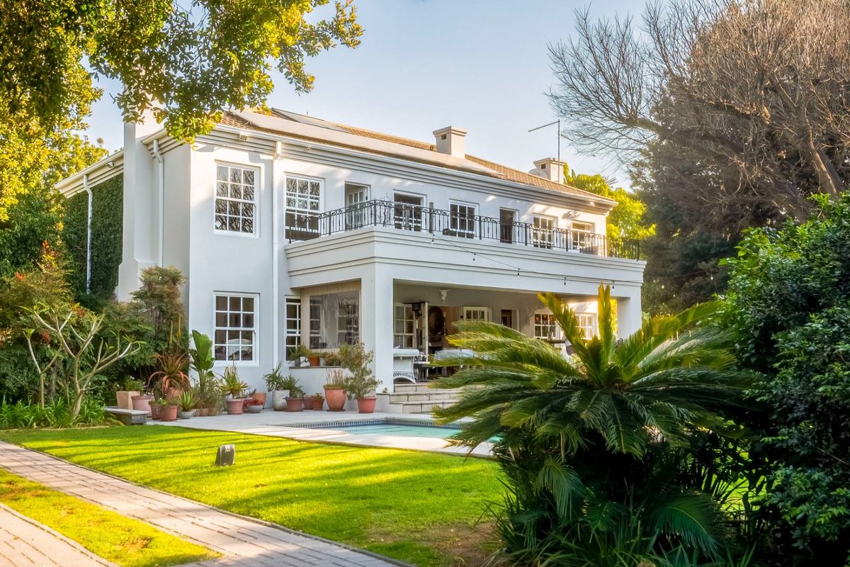 A well-maintained two-story rear elevation featuring a swimming pool, paved patio area, and an upper-level balcony with wrought iron railings.