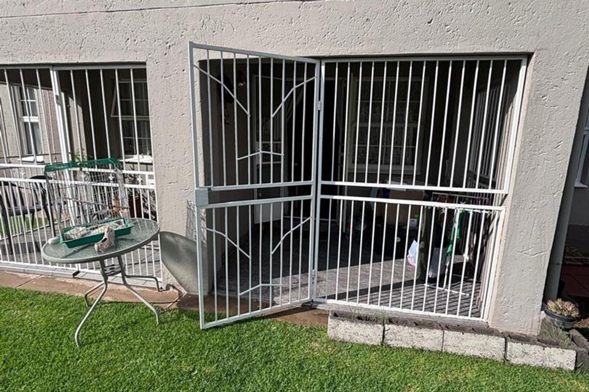 Rear exterior view of the townhouse featuring a small lawn area and a white metal security gate providing access to the interior.