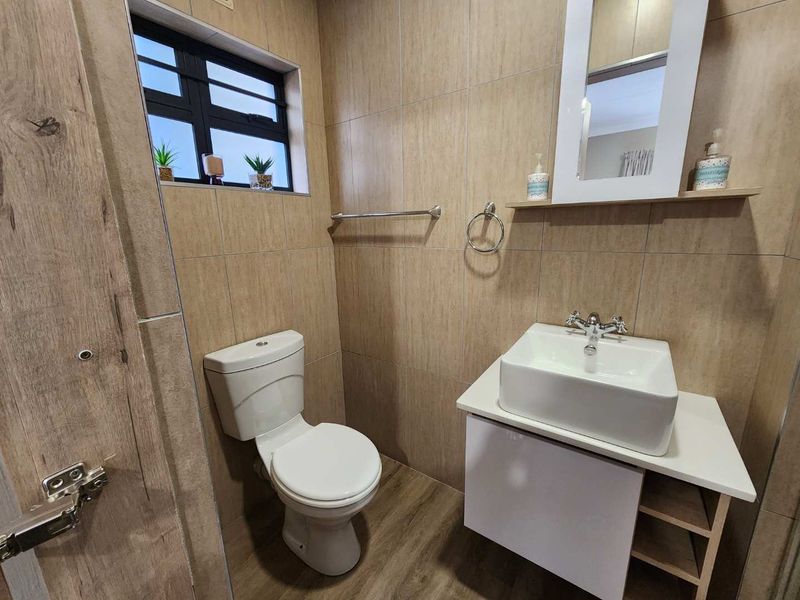 A modern bathroom featuring wood-look floor tiles, full-height wall tiling, a contemporary vessel sink vanity, and a toilet.