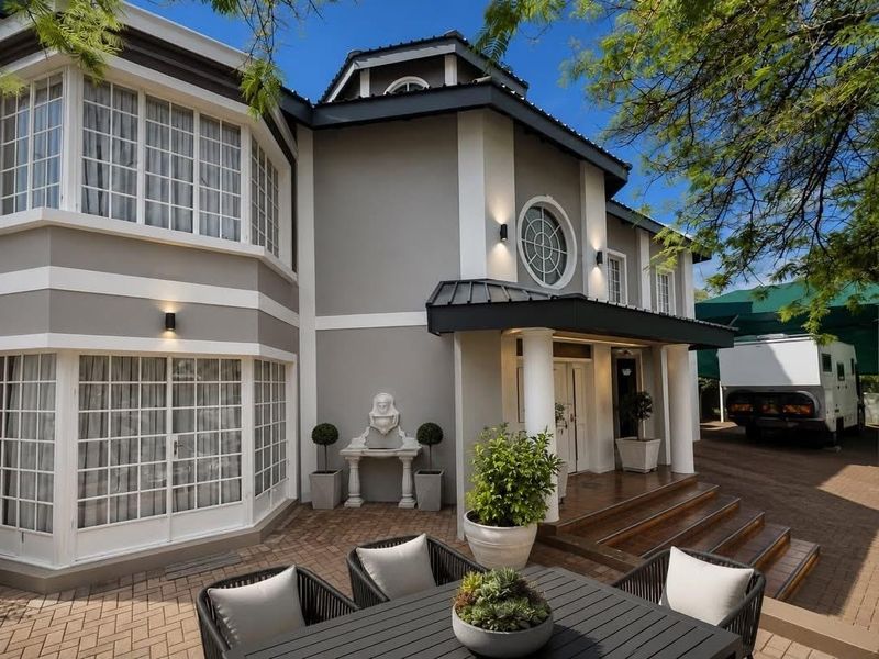 A well-maintained rear exterior featuring a paved patio area, decorative wall fountain, and elegant architectural details including bay windows and a circular feature window.