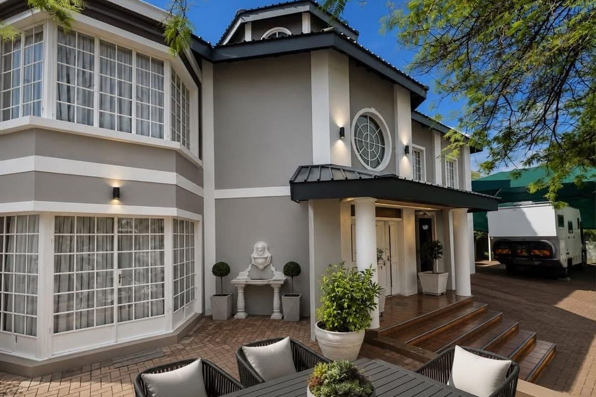 A well-maintained rear exterior featuring a paved patio area, decorative wall fountain, and elegant architectural details including bay windows and a circular feature window.