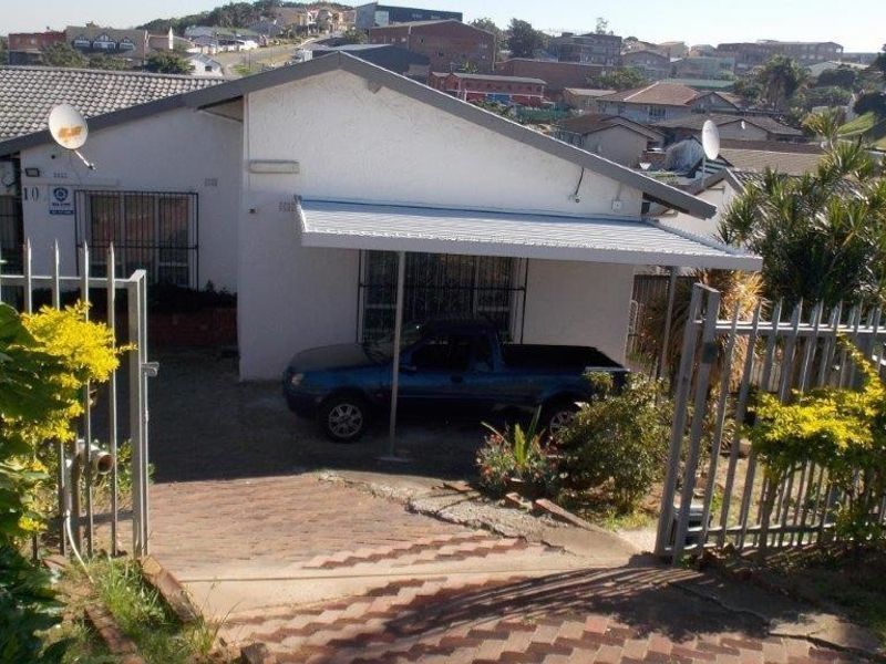 Front exterior view of a residential house featuring a paved driveway, metal security gate, and a covered carport area.