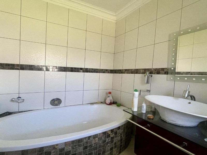 A functional bathroom featuring a built-in bathtub, a modern vessel sink on a vanity cabinet, and decorative mosaic tile accents.