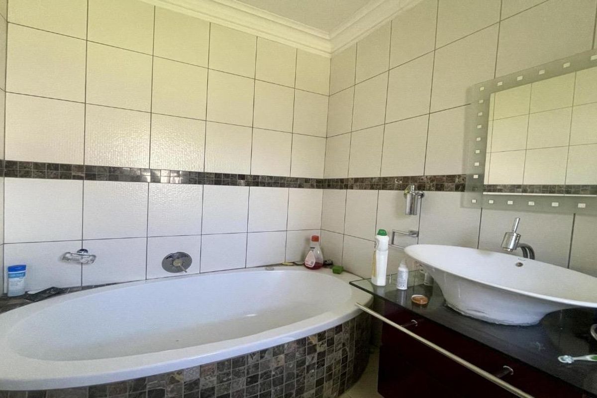 A functional bathroom featuring a built-in bathtub, a modern vessel sink on a vanity cabinet, and decorative mosaic tile accents.