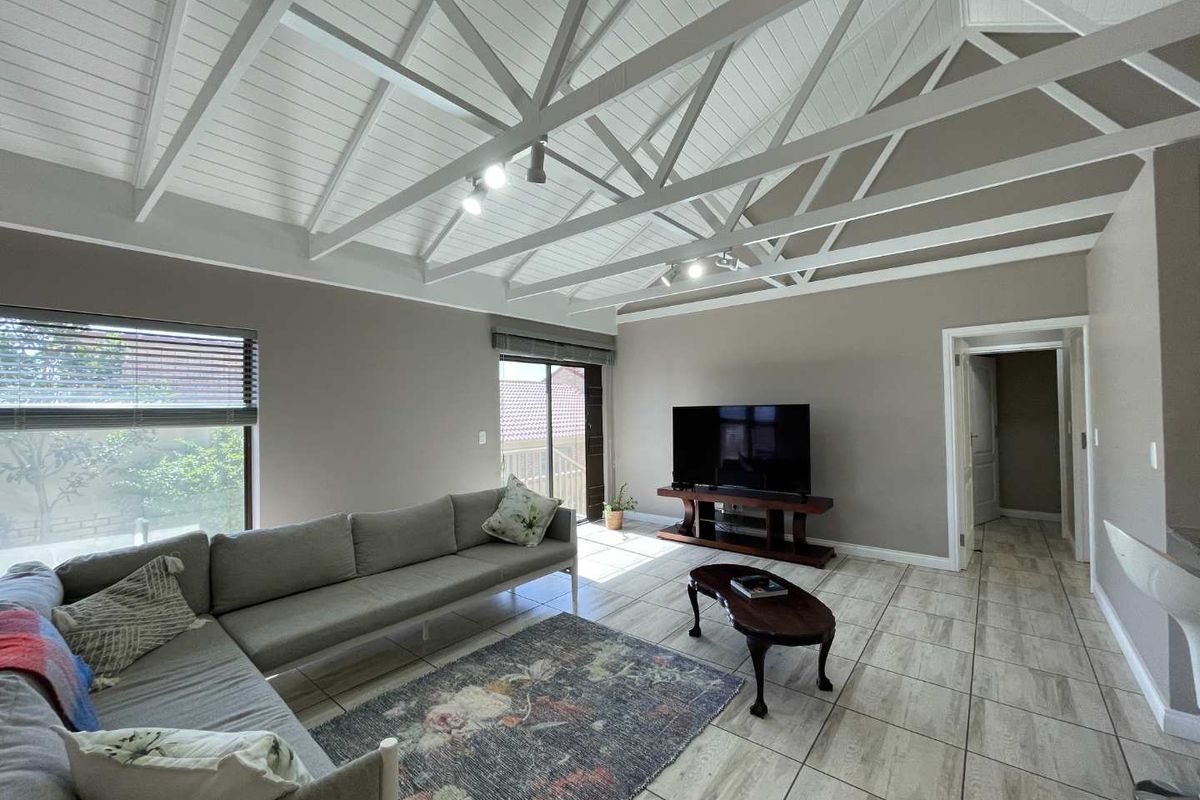 Spacious living room featuring a high vaulted ceiling with exposed white timber trusses, tiled flooring, and large sliding glass doors providing natural light.