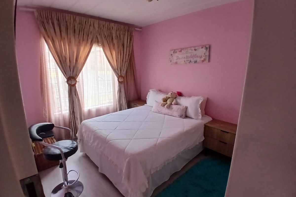 A bedroom featuring laminate flooring and curtain rails, currently styled with pink wall paint.