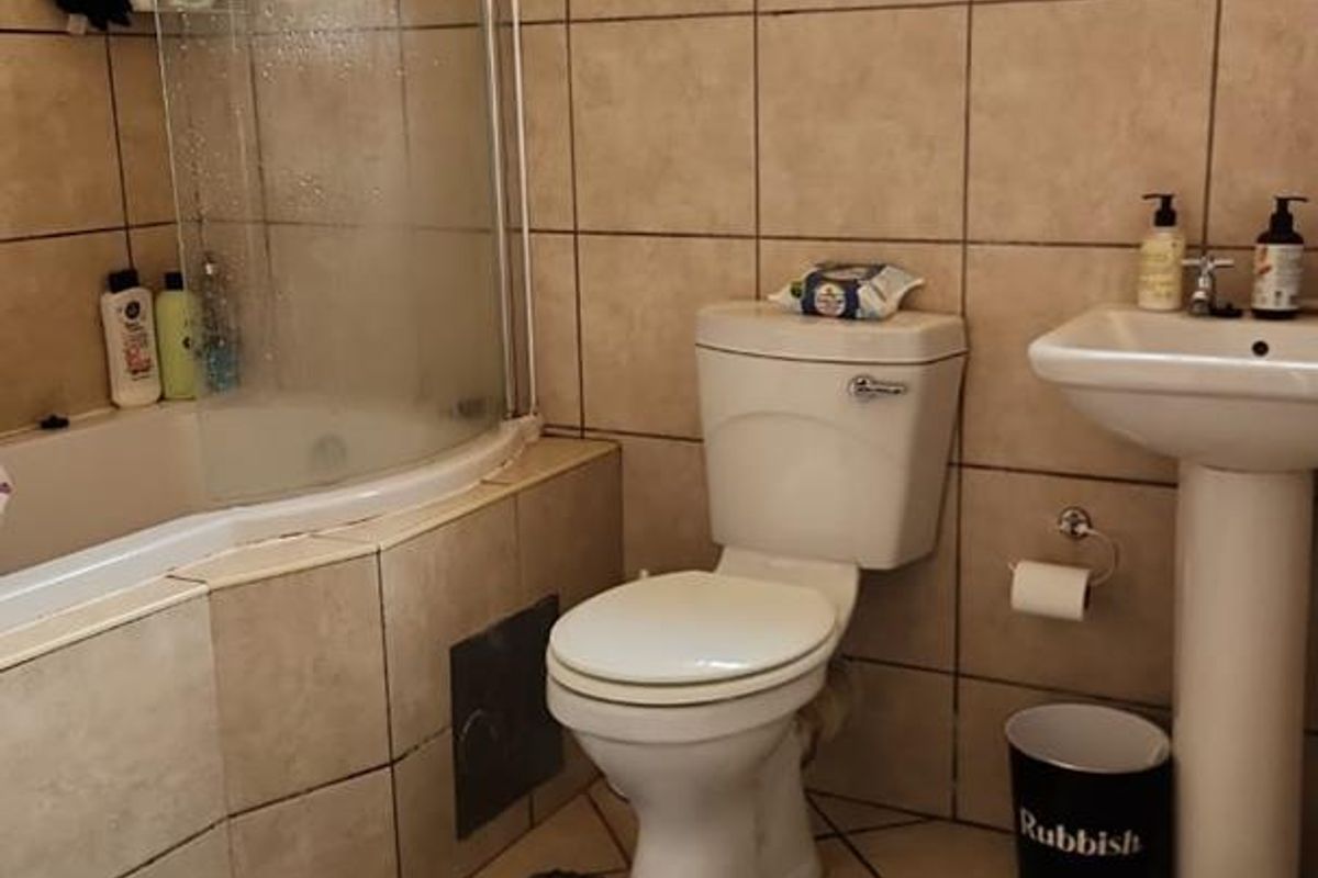 A functional bathroom featuring a tiled shower-over-bath combination, pedestal basin, and toilet with neutral wall and floor tiling.