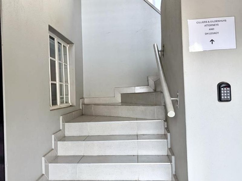 A clean, tiled staircase entry area featuring a security keypad and a unique diamond-shaped window, providing access to office suites.