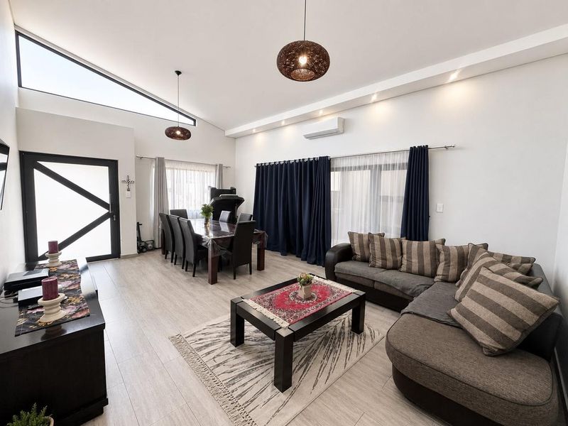 Spacious open-plan living and dining area featuring high raked ceilings, modern tiled flooring, recessed lighting, and a split-system air conditioner.