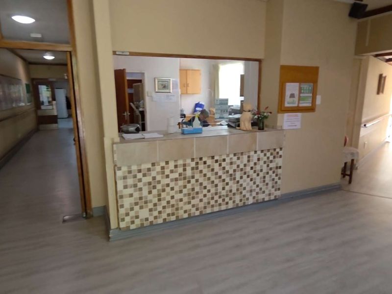 A functional reception area featuring a tiled service counter, laminate flooring, and access to connecting hallways in a commercial or residential facility.