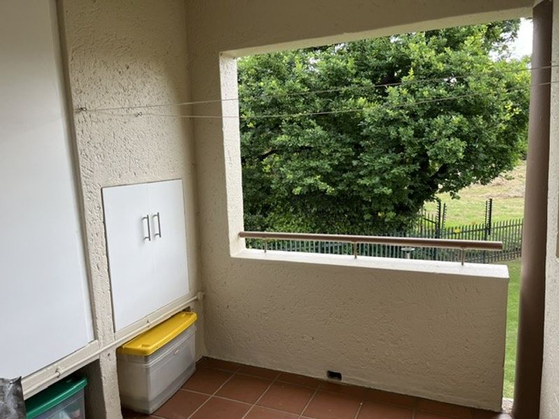 A functional balcony area featuring built-in storage cabinetry, tiled flooring, and a metal balustrade overlooking a green garden space.