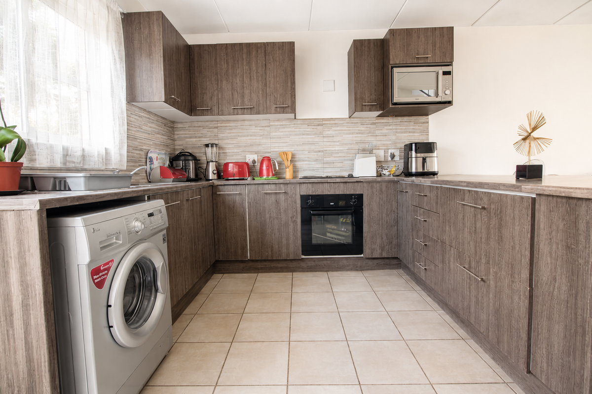A functional kitchen featuring wood-grain cabinetry, tiled backsplash, built-in oven, and integrated space for a washing machine.