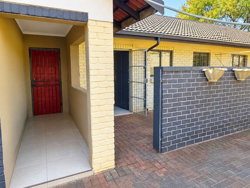 Front entrance area featuring brick paving, a covered tiled porch, and a secure gated entry point with a brick boundary wall.
