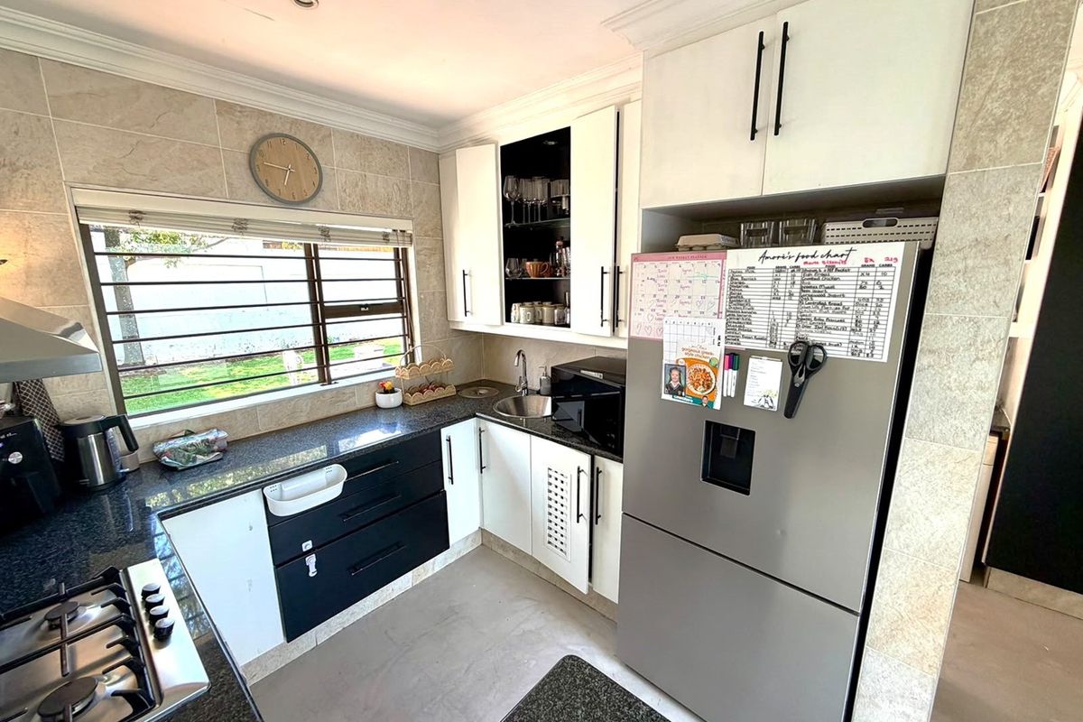 A compact kitchen featuring granite countertops, white and black cabinetry, a gas hob with extractor, and tiled wall finishes.