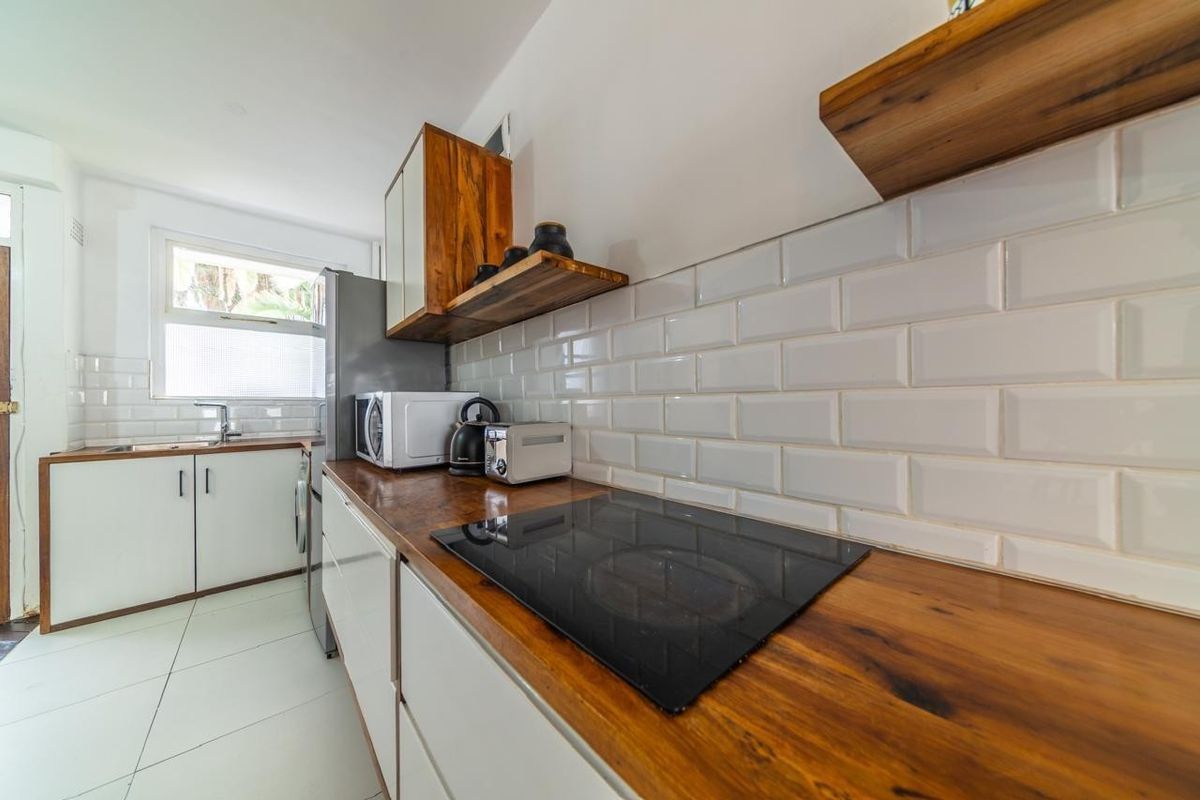 A modern kitchen featuring wooden countertops, white cabinetry, subway tile backsplash, and a built-in electric hob.