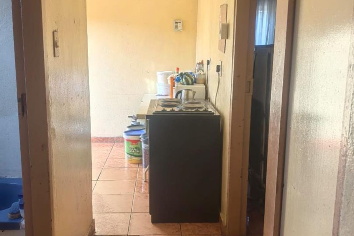 A functional kitchen area featuring tiled flooring and a built-in stove, accessible via a hallway with dated finishes.