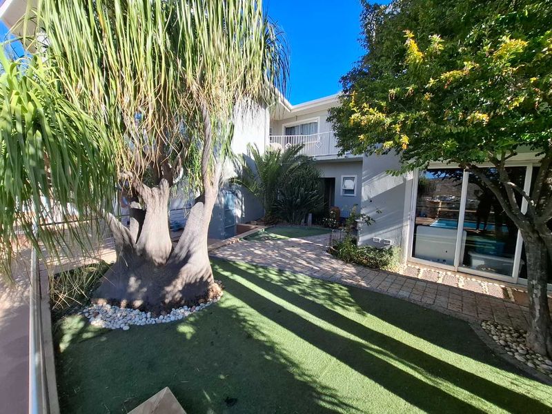 A well-maintained rear courtyard featuring a paved walkway, artificial lawn, mature trees, and sliding glass doors leading into the townhouse.