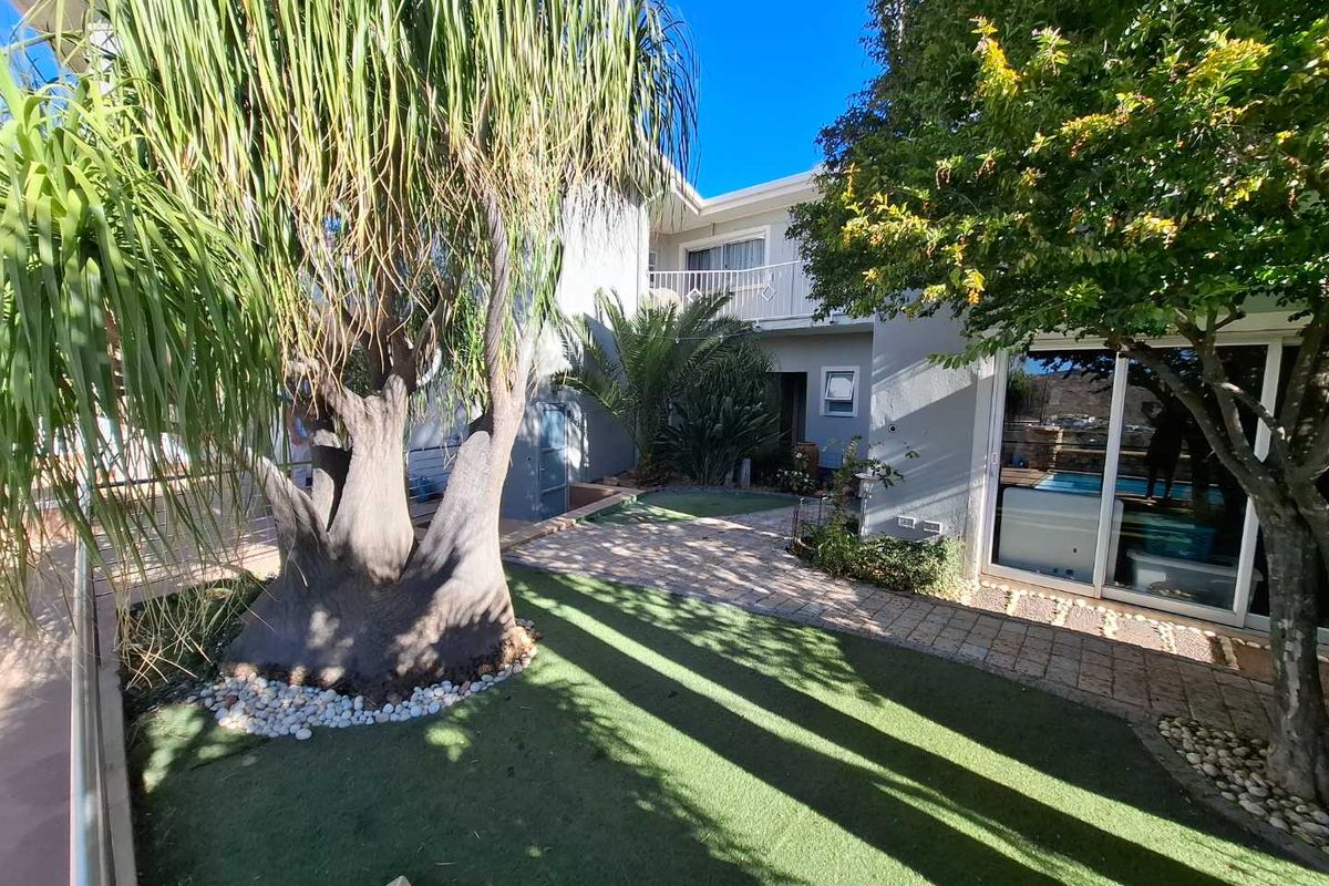 A well-maintained rear courtyard featuring a paved walkway, artificial lawn, mature trees, and sliding glass doors leading into the townhouse.