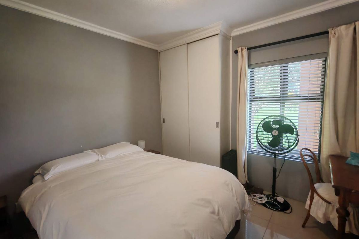 A bedroom featuring built-in cupboards, tiled flooring, and a window with blinds, providing a functional and comfortable living space.