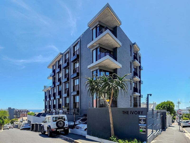 Modern multi-story apartment building exterior featuring contemporary architectural design, private balconies, and secure perimeter fencing.