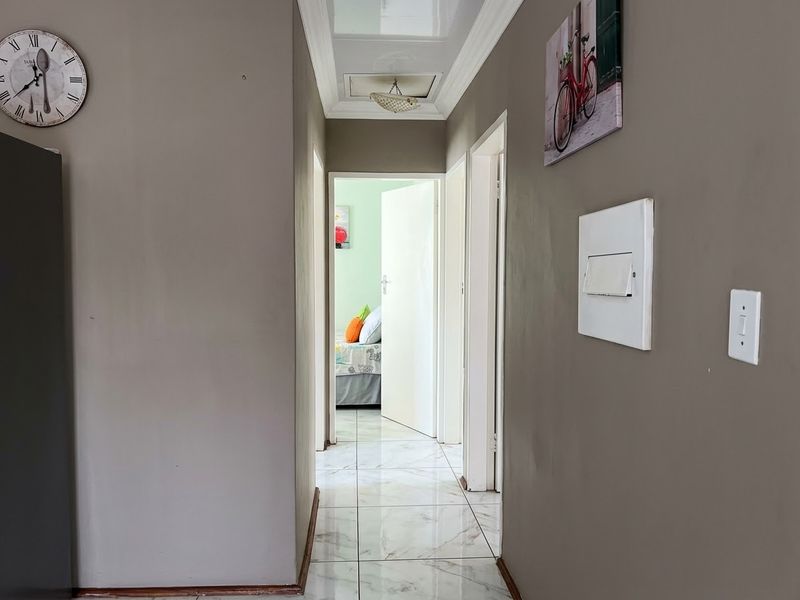A clean, tiled hallway providing access to multiple rooms, featuring neutral wall tones and a ceiling access hatch.
