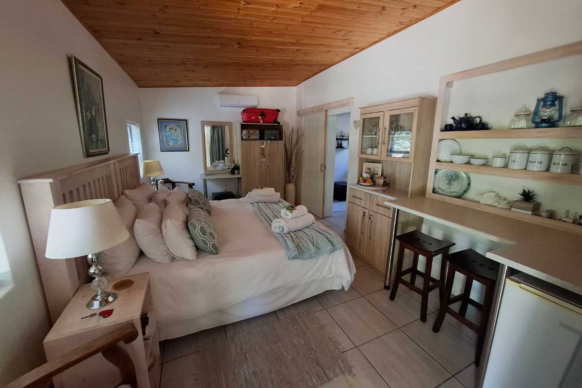 A compact bedroom featuring a wooden tongue-and-groove ceiling, tiled flooring, and a built-in kitchenette area with shelving and cabinetry.