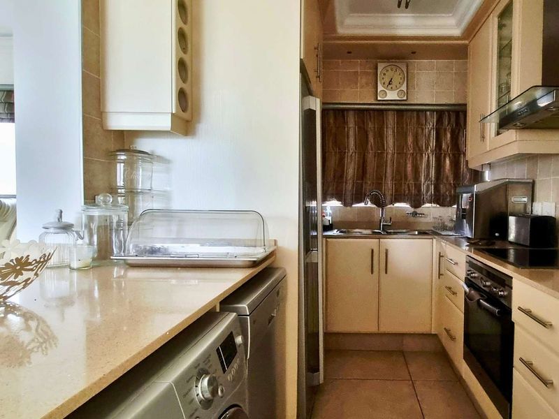 A functional kitchen featuring light-toned cabinetry, stone countertops, integrated oven and hob, and tiled backsplash, offering a practical layout for daily meal preparation.