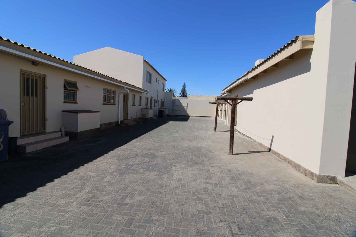 A paved exterior courtyard area between apartment building wings, featuring exterior access doors, security gates, and a fixed wooden washing line structure.