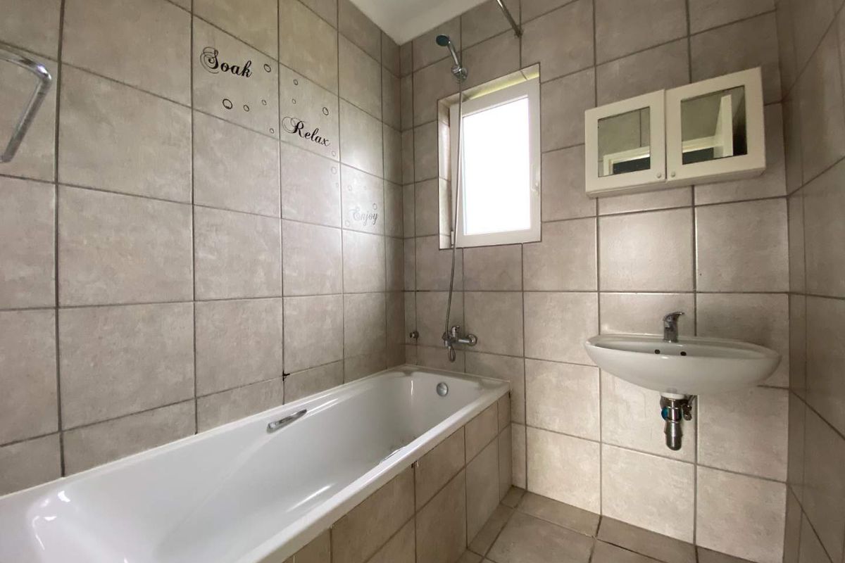 A functional bathroom featuring a built-in bathtub with shower mixer, wall-mounted basin, and tiled walls and flooring.