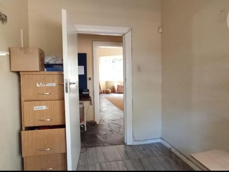 A small office space featuring tiled flooring and a doorway leading to an adjacent room, requiring minor cosmetic updates to improve its appeal.