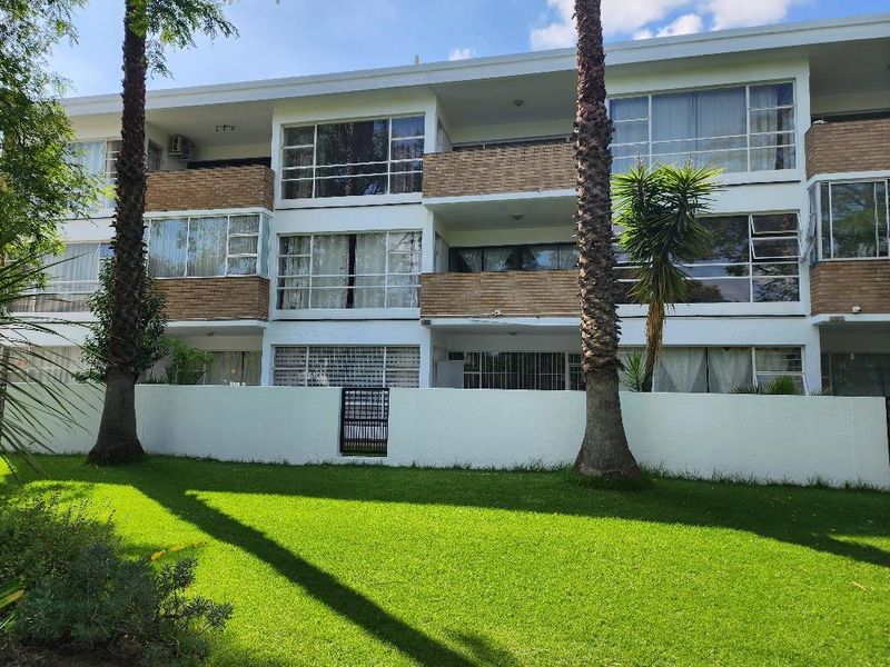 Rear view of a multi-story apartment building featuring brick facade, private balconies, large windows, and a well-maintained communal garden area.